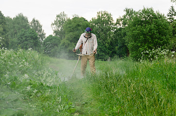Image showing Worker man cut trim mow wet grass after rain 