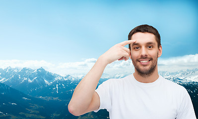 Image showing smiling young handsome man pointing to forehead