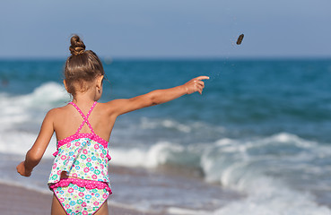 Image showing Little girl throws rocks into the sea