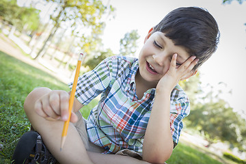 Image showing Frustrated Cute Young Boy Holding Pencil Sitting on the Grass