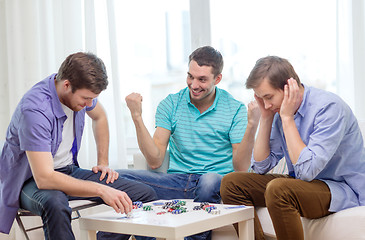 Image showing happy three male friends playing poker at home