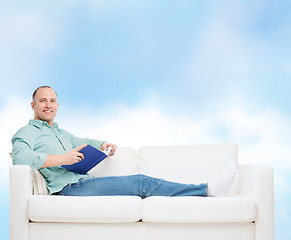 Image showing smiling man lying on sofa with book