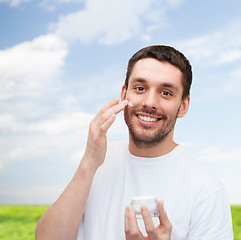 Image showing beautiful smiling man applyin cream