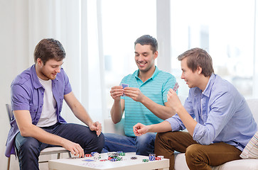 Image showing happy three male friends playing poker at home