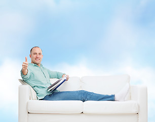 Image showing smiling man lying on sofa with book