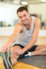 Image showing smiling man stretching on mat in the gym