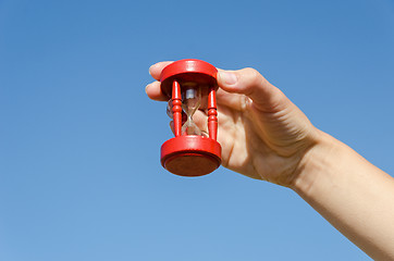 Image showing red old hourglass in hand on blue sky background 