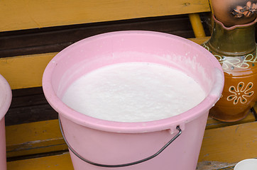 Image showing pink bucket full of cow milk on wooden bench 