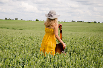 Image showing back view of women with guitar in wide rye field  