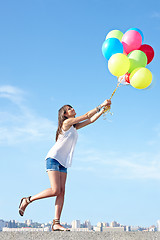 Image showing Happy young woman flying away with balloons