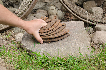 Image showing man hand put iron horseshoe pile on stone outdoor 