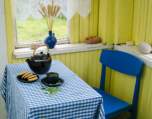 Image showing teapot with tea cup and cookie on table blue chair 