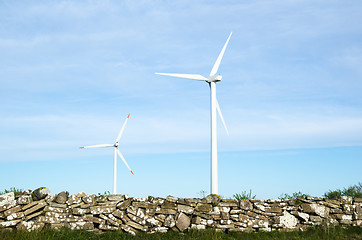 Image showing Two wind turbines by an old traditional stonewall at the swedish