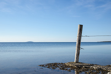 Image showing Weathered old wooden pole by a flat rock coast