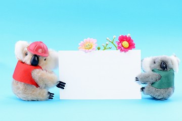 Image showing Two toy koala holding a blank white card