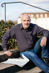 Image showing Man sitting on steps reading a newspaper