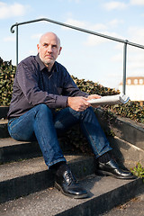 Image showing Man sitting on steps reading a newspaper