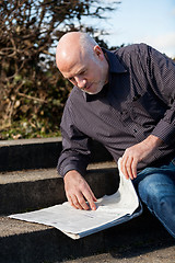 Image showing Man sitting on steps reading a newspaper