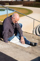 Image showing Man sitting on steps reading a newspaper