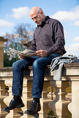 Image showing Man sitting reading a newspaper on a stone wall