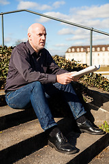 Image showing Man sitting on steps reading a newspaper