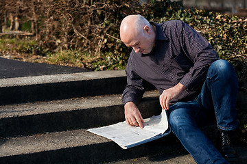 Image showing Man sitting on steps reading a newspaper