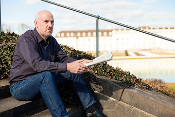 Image showing Man sitting on steps reading a newspaper