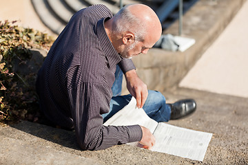 Image showing Man sitting on steps reading a newspaper