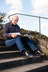 Image showing Man sitting on steps reading a newspaper