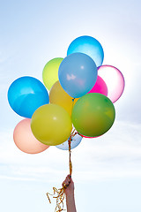 Image showing Hand holding bunch of colorful balloons in blue sky