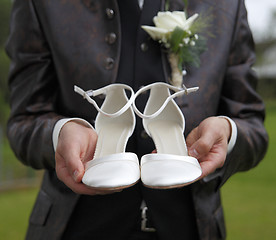 Image showing Groom is holding bridal shoes