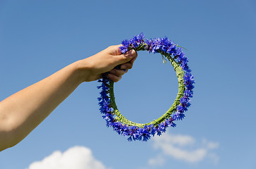 Image showing hand hold cornflower crown in blue sky background