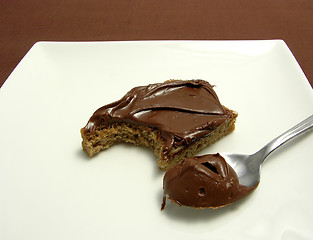 Image showing Bitten into a wholemeal bread with hazelnut spread on a plate with little spoon