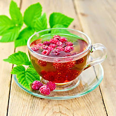 Image showing Tea with raspberries in glass cup on board