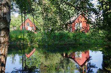 Image showing red rural home reflected through branches on pond 