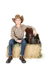 Image showing Boy on hay bale with saddle