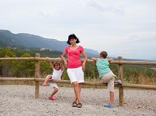 Image showing Mother and two children leaning on a fence