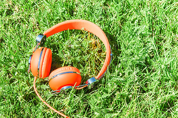 Image showing Bright orange colorful headphones on fresh sward