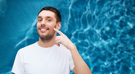 Image showing smiling young handsome man pointing to cheek