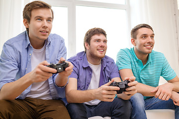 Image showing smiling friends playing video games at home