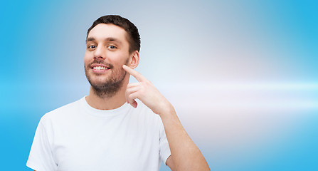 Image showing smiling young handsome man pointing to cheek