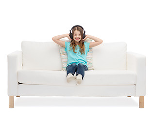 Image showing smiling little girl in headphones sitting on sofa