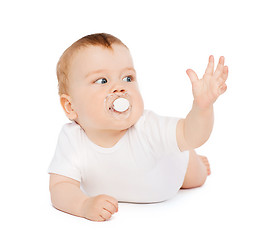 Image showing smiling baby lying on floor with dummy in mouth