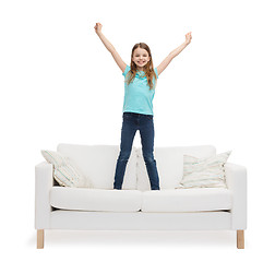 Image showing smiling little girl jumping or dancing on sofa