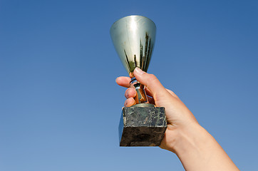 Image showing female hand hold award cup on blue sky background 