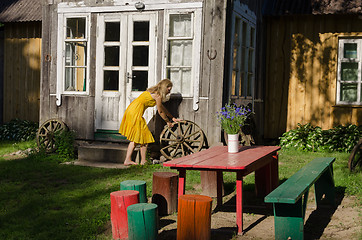 Image showing Rural house yard and girl roll old carriage wheel 