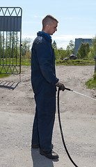 Image showing Worker in overalls watering area with water from a hose 