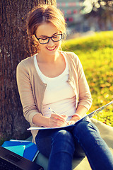 Image showing smiling teenager in eyeglasses writing in notebook