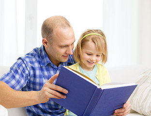 Image showing smiling father and daughter with book at home