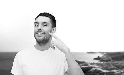 Image showing smiling young handsome man pointing to cheek